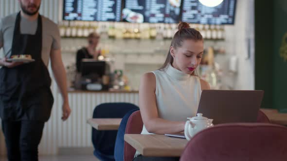 Attractive Longhaired Girl Works with Laptop in Cafe Waiter Brings Her Cake