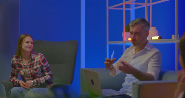 Grayhaired Male Blogger Sits with a Laptop and Emotionally Tells Everyone Having Fun alt