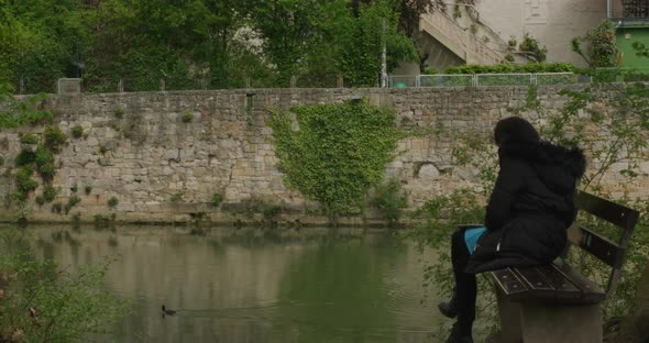 Stylish woman on bench calmly watching duck passing by in Tubingen downtown river in Balvaria, Germa alt