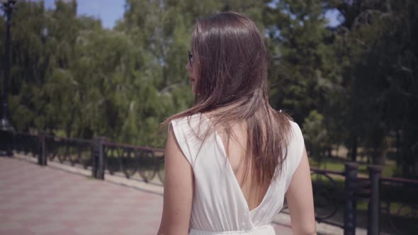Portrait Glamorous Young Girl Wearing Sunglasses and a Long White Summer Fashion Dress Walking alt