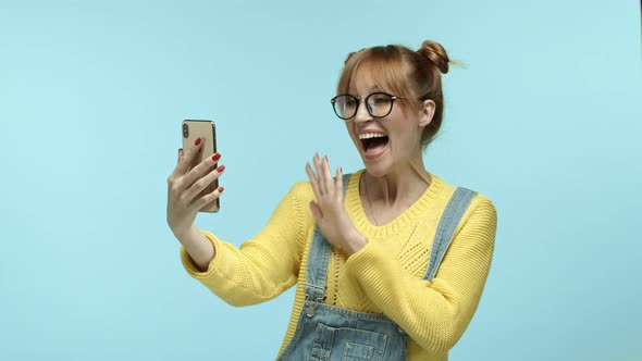 Young Woman in Glasses Talking Via Video Call on Smartphone Saying Hi and Waving Hand at Phone