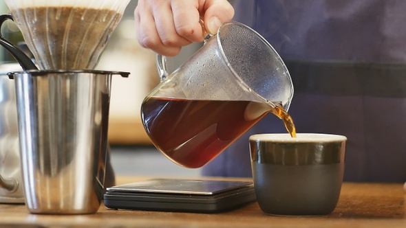 Pouring hot coffee to a black cup