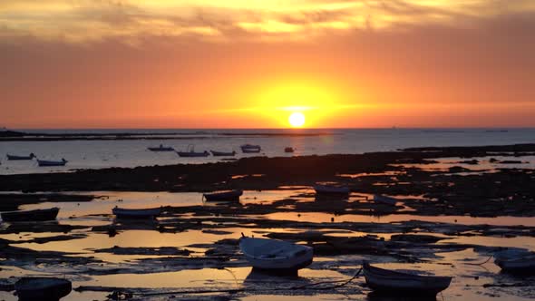 Slow tilt up over small fishing boats parked at low tide during sunset alt
