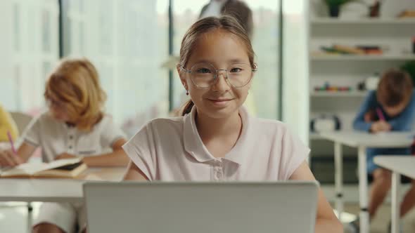Portrait of the Asian Smiled Girl Sitting on the Desk with Laptop in a Class During Computer Science alt