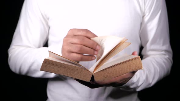 Young Man Turning Pages of a Book Isolated on Black alt