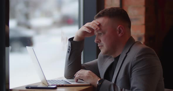 Man Exploring Work Online Sitting In Cafe, Focused. Browse Information On Laptop Screen