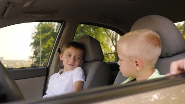 Two Cute Little Boys are Sitting at the Wheel of Their Father's Car and Talking alt