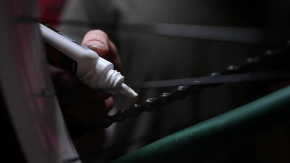 Closeup of Unrecognizable Skilled Repairman Greasing Oiling Lubricating Links of Bicycle Chain alt