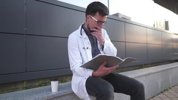 Young Male Doctor Works With Medical Documents During Coffee Break In