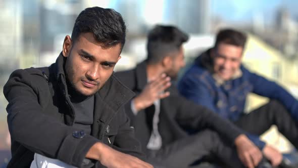 Young Sad Middle Eastern Man Looking at Camera As Blurred Friends Laughing Pointing Mocking at alt