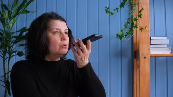 Middle Aged Old Woman Hold Phone Speak Activate Virtual Digital Voice Recognition Assistant at Home alt