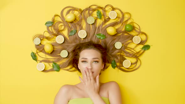 beautiful girl lying on colored background with citrus fruits fruits on long hair, female flirting