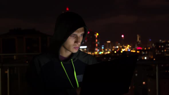 Young Man Using Laptop on Balcony at Night