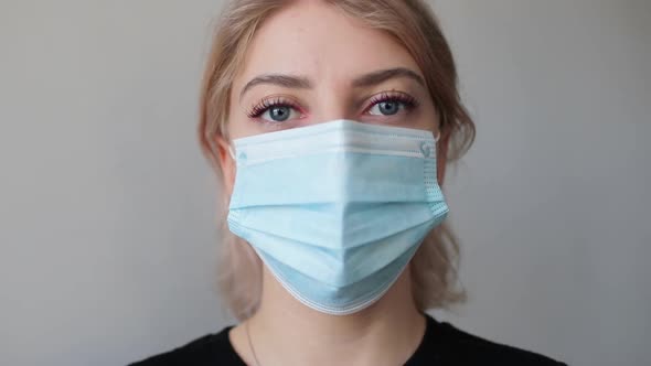 Young woman standing and looking at the camera wearing medical mask at home