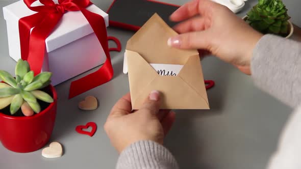 Woman opening an envelope with BE MY VALENTINE card near valentine's day present alt