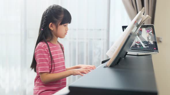 Homeschool Asian little young kid girl learning piano by watch music online instruction from tablet alt