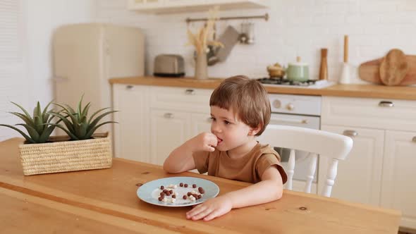 a Little Caucasian Boy Eats Krunchy Breakfast and Enjoys It at Kitchen Table alt