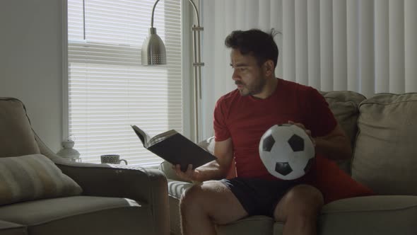 Man Holding Soccer Ball Reading About Plays in Book and Imagining a Goal alt