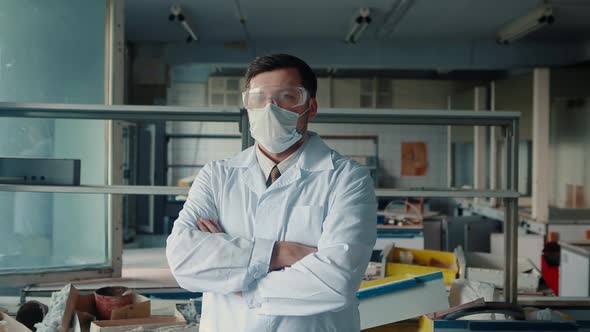 A male doctor with a protective mask is standing in front of a camera in a destroyed lab.