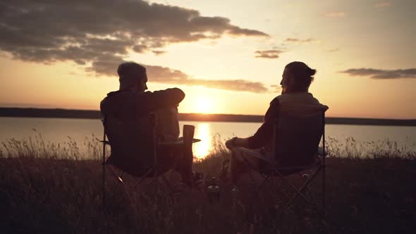 Two Men Friends Camping Near a River During Sunset Passing Food From a Parcel alt