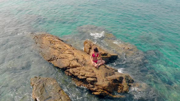 Girl in Red Bikini Sits on Huge Stone in Sea Waving Hand alt
