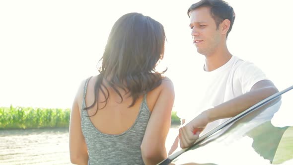 Couple leaning against car, talking and laughing