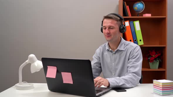 A Young Worker Communicates with a Client at an Online Conference From the Office Through Headphones alt