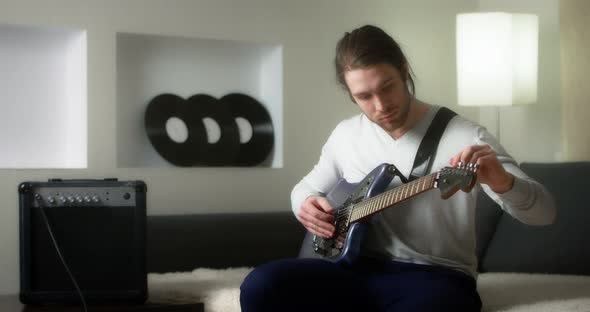 Creative Musician in a Gray Jumper Tunes a Blue Electric Guitar