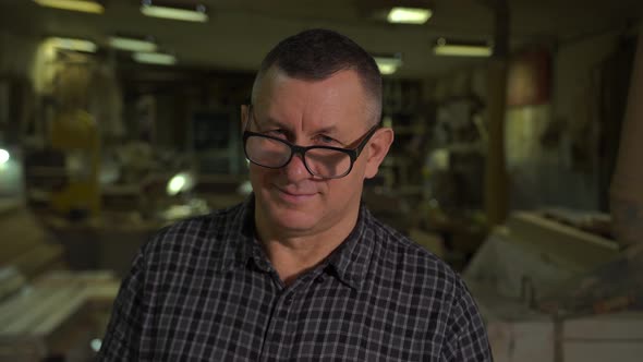 Engineer at a Furniture Factory Looks at the Camera and Puts Glasses on His Face