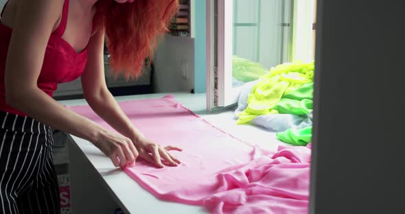 Female Dressmaker Measuring a Pink Silk with Ruler on Surface in Atelier alt