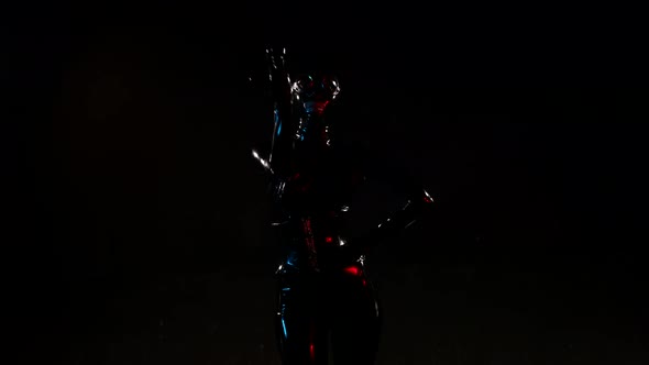 a Woman in a Black Latex Suit and Helmet Poses Against a Dark Background alt