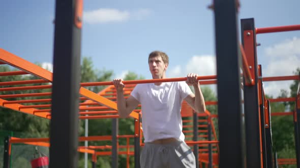Confident Young Sportsman Doing Pullups on Gymnastic Bar Outdoors in Sunshine alt