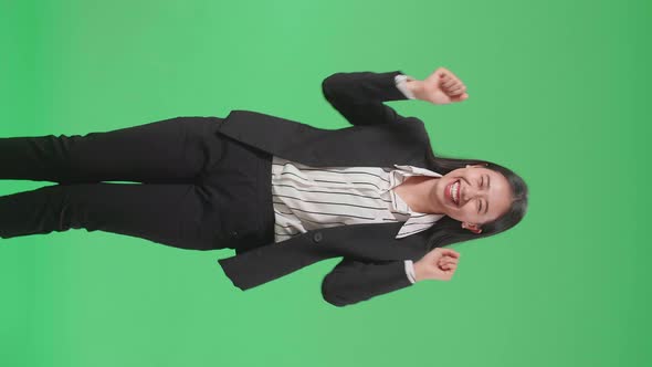 A Smiling Asian Business Woman Dancing While Standing On Green Screen Background In The Studio alt