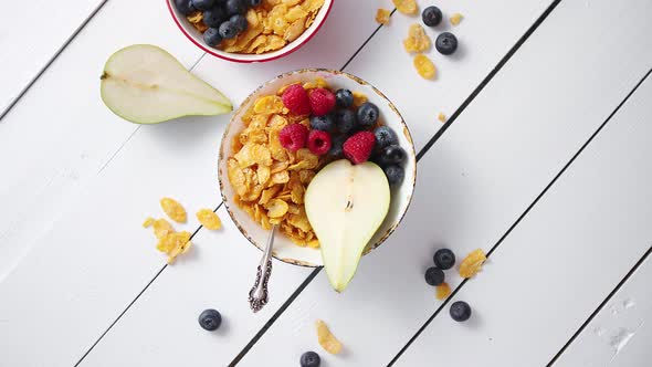 Golden Cornflakes with Fresh Fruits of Raspberries, Blueberries and Pear in Ceramic Bowl alt