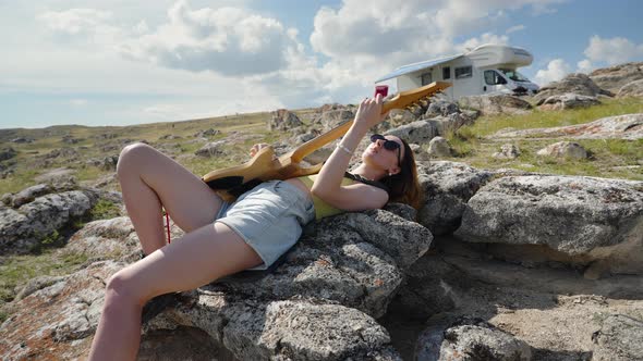 Young Woman Playing Guitar and Singing Near RV Camping in Summer