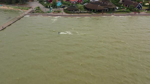 AERIAL: Pro Kite Surfer is Riding on Green Sea and Jumps Over Stone Pier alt