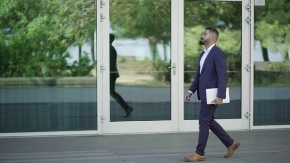 Handsome Bearded Businessman Walking with Laptop on Street alt