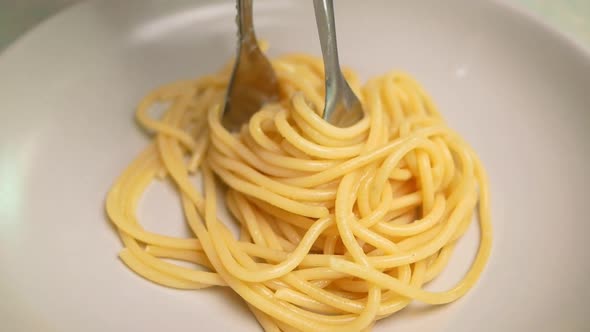 Close-up shot of hand holding a tong picking up cooked spaghetti placing on a plate. alt