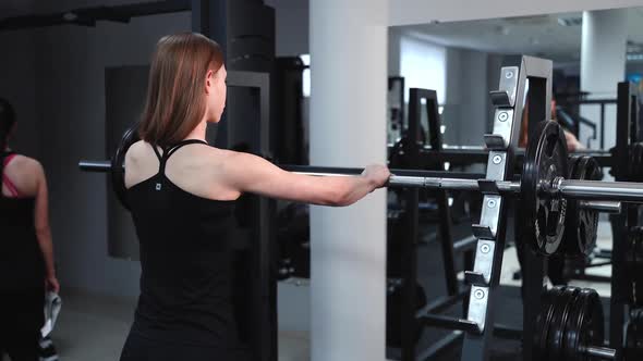 Athletic young woman walks up to the weight bar and lifts her in the fitness club alt