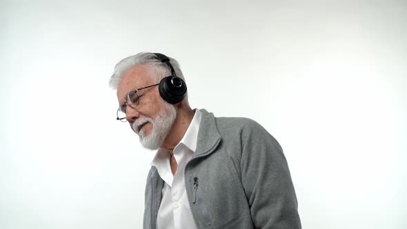 Stylish Emotional Old Man with a Gray Beard and Headphones Listens to Modern Music and Dances on a