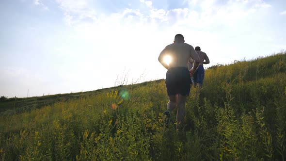 Group of Young Men Running Up the Green Hill Over Blue Sky with Sun Flare at Background. Male alt
