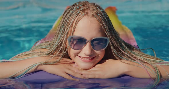 Girl with Afro Pigtails Swims on an Inflatable Mattress in the Pool Resting and Enjoying the Rest alt