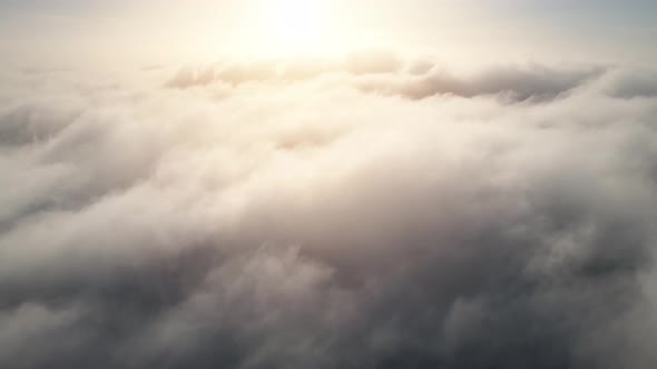 Aerial shot of flying over a layer of soft clouds at dawn alt