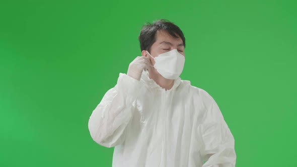 Asian Male Wear Protective Uniform PPE Take Off Glasses, Mask And Smile In Green Screen Studio alt