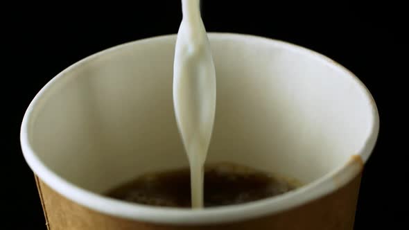 Spilling milk into a coffee drink. Black background. Close-up.