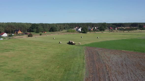 Aerial Agricultural shot of a Tractor carrying a trailer with bales of hay entering a field to colle alt