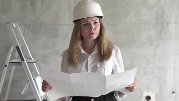The girl engineer builder is checking the drawings at the apartment of the projected house. alt