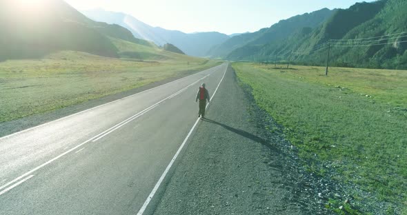 Flight Over Hitchhiker Tourist Walking on Asphalt Road. Huge Rural Valley at Summer Day. Backpack alt