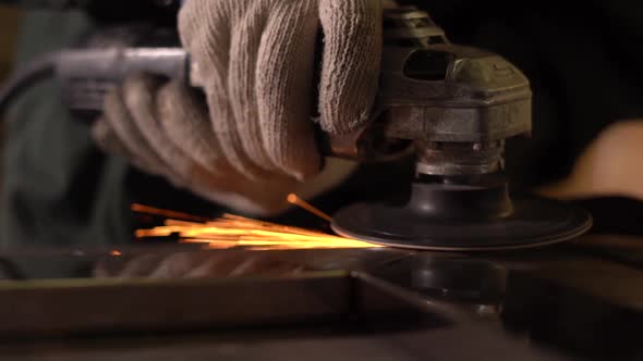 Male Worker Polishing Metal Part With Grinder. Sparks Fly Into the Camera. The Camera Moves From