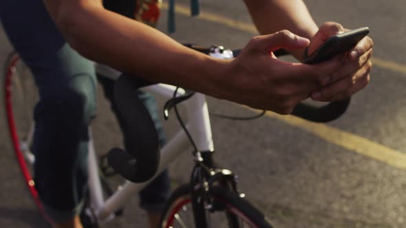 African american man in city, sitting on bike in street using smartphone alt